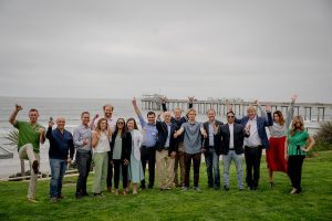 Group of people posing on a lawn with the ocean and Scripps Pier in the background.